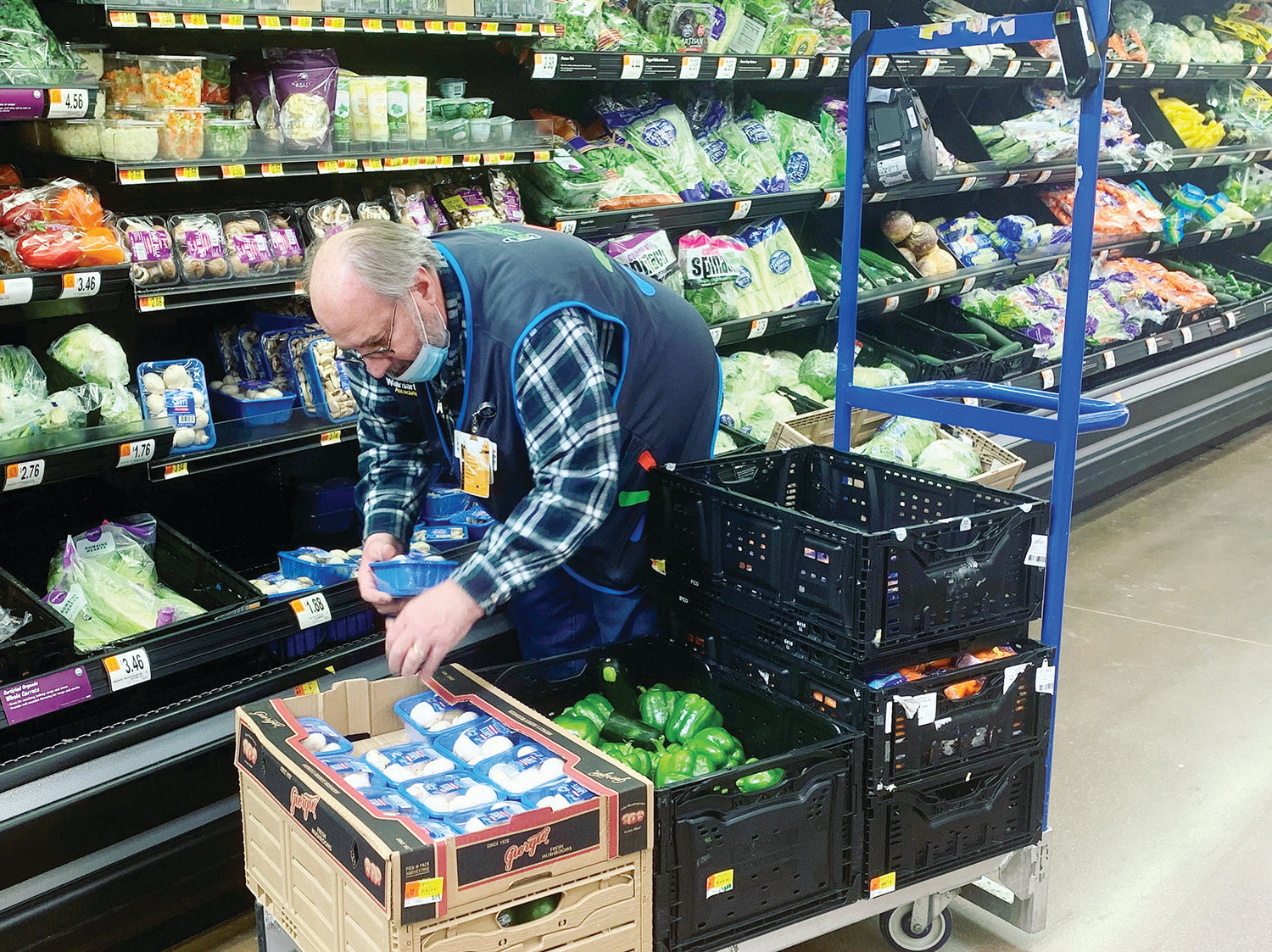 A worker at the Delta Township Marketplace Walmart places produce with his mask not concealing his nose and only partially covering his mouth.
