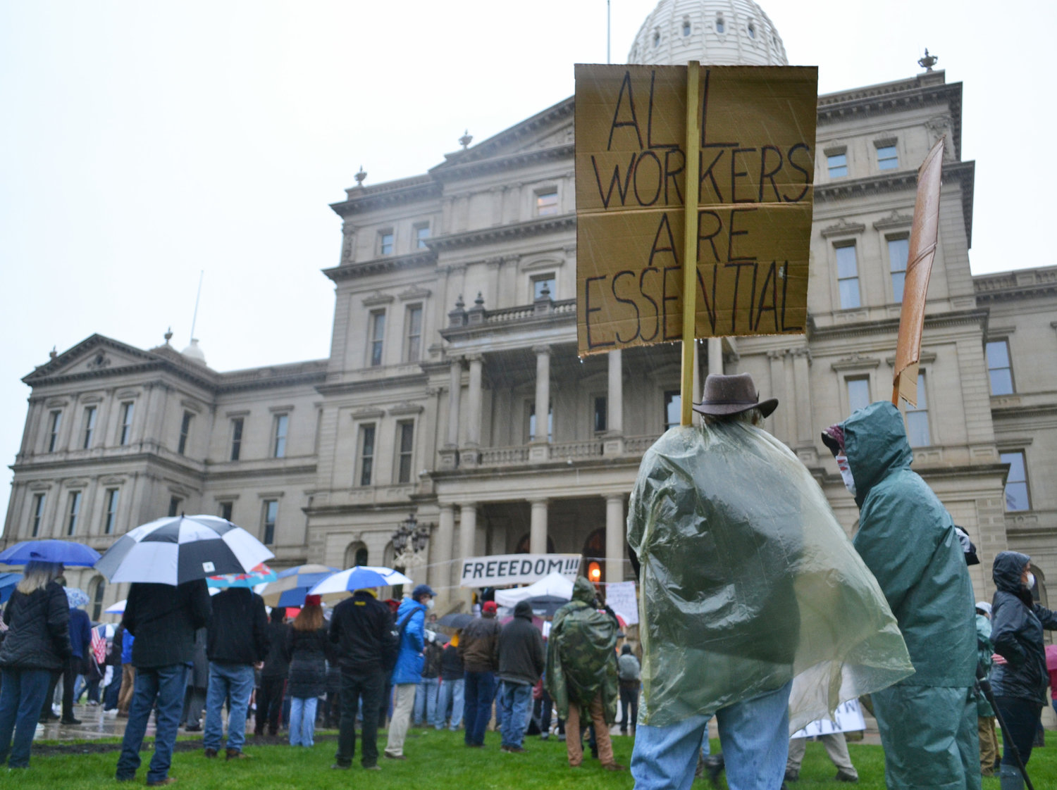 A protester in the rain carrying a sign reading, "All workers are essential."