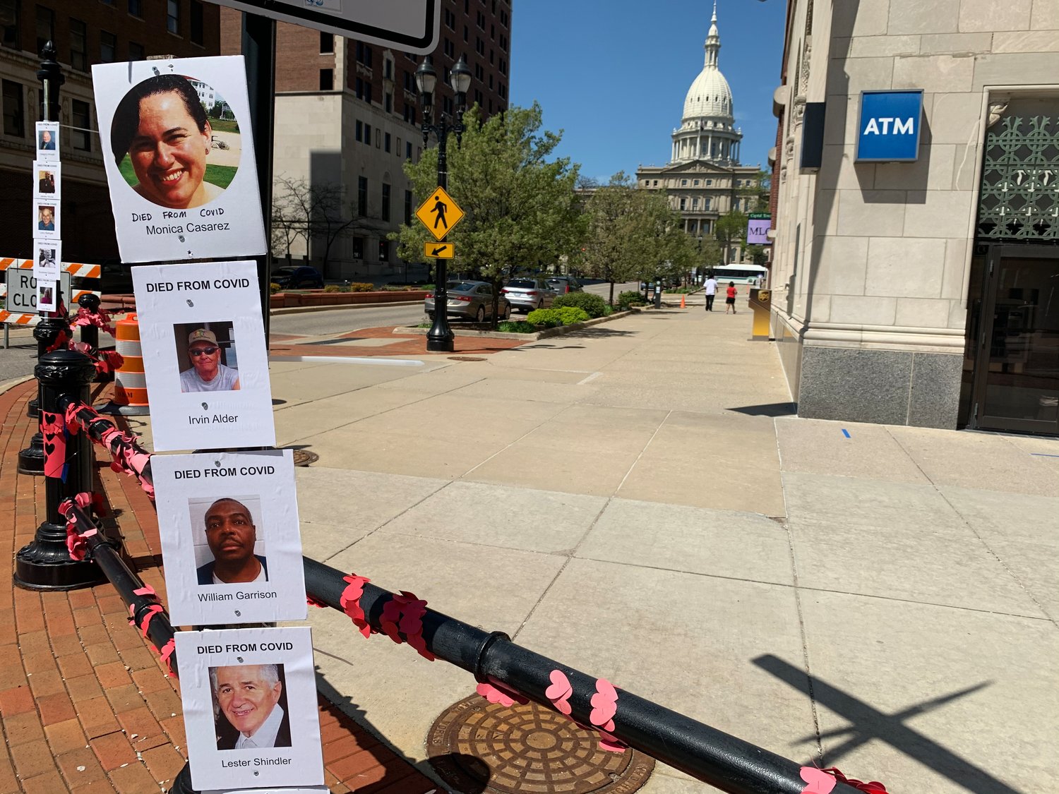 Posters of people who have succumbed to COVID-19 in Michigan stuck to a post at the intersection of Washington Square and Michigan Avenue today.