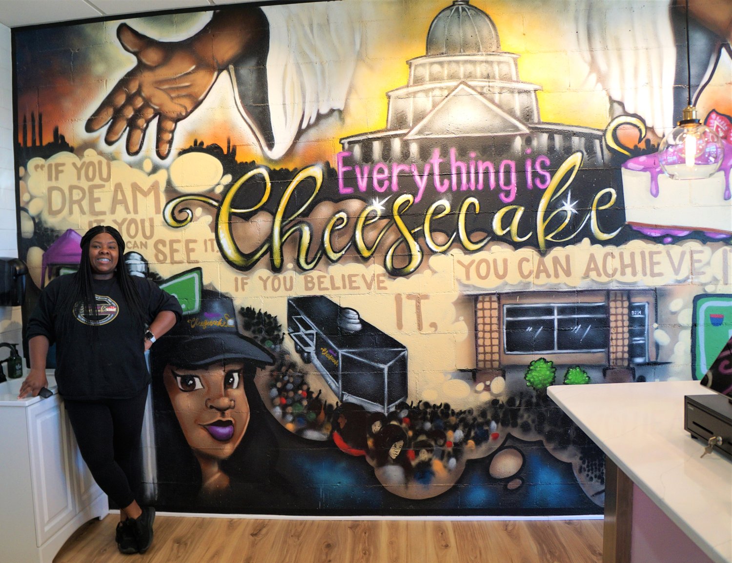 Deanna Brown poses next to her business’ mural, which details her journey running Everything is Cheesecake. The new shop celebrated its grand opening May 7. The former food truck has grown a local following in Lansing thanks to word-of-mouth fanfare.