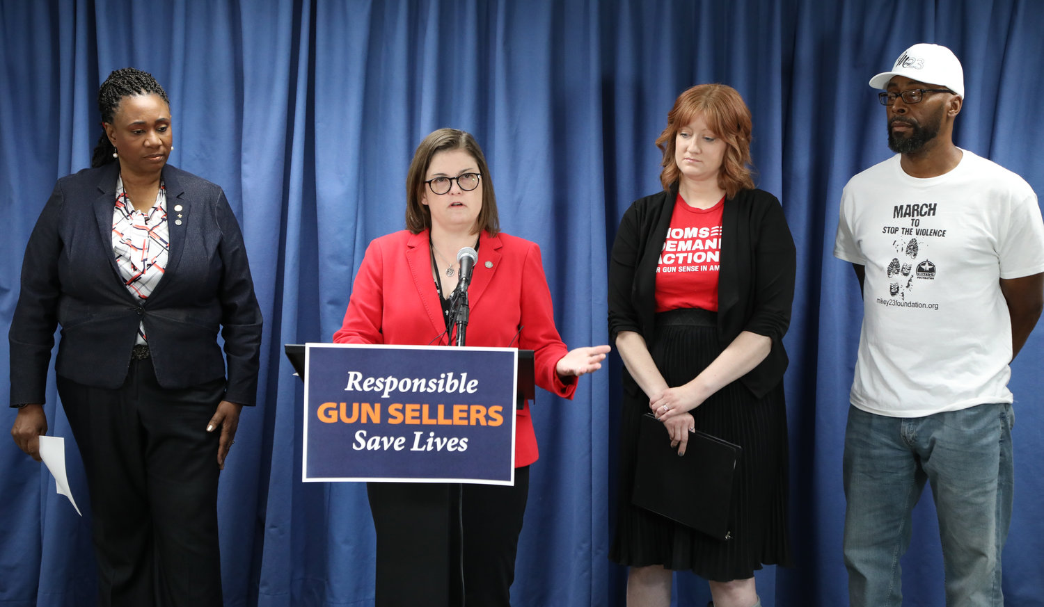 State Rep. Kara Hope, D-Holt, (in red jacket) announces legislation to tighten security at gun shops.  On her left is Rep. Stephanie Young, D-Detroit; to her right are the Rev. Christin Fawcett of Moms Demand Action and Grace Lutheran Church and Michael McKissic of the Mickey23 Foundation in Lansing.