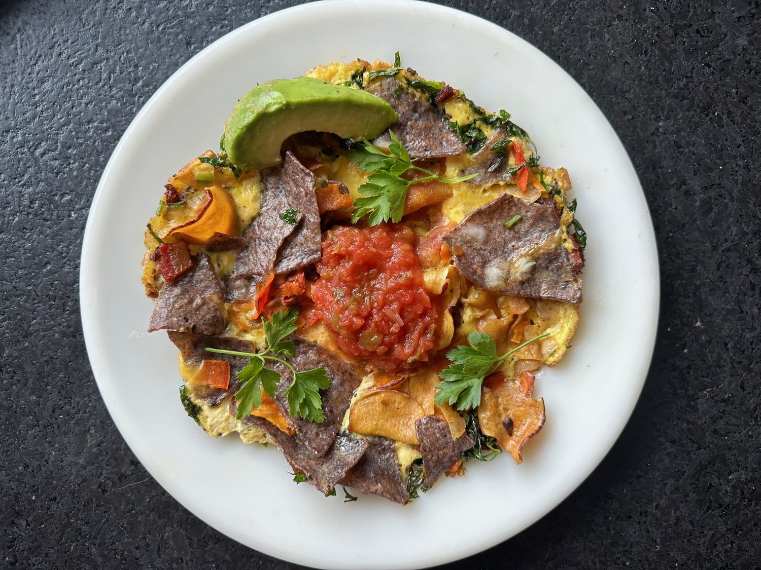 Migas, an egg-based dish originating in southern Spain and Portugal, can be made in a number of ways. This version includes bacon, garlic, parsley, cheese, tortilla chips, vegetable chips and a dollop of salsa to top it all off.