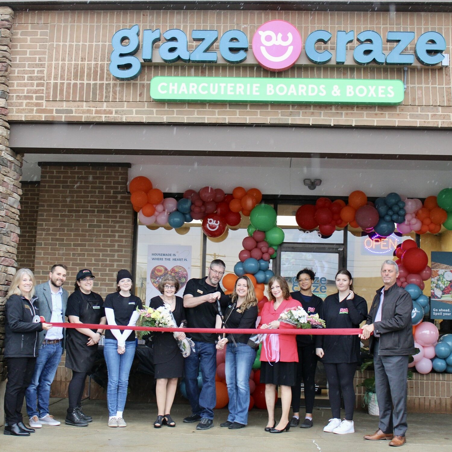 Husband-and-wife team Silas and Lindsey Coffelt, alongside their moms and the Lansing Regional Chamber of Commerce, welcomed the newest Graze Craze location to Okemos Friday (April 28) with a ribbon-cutting ceremony.