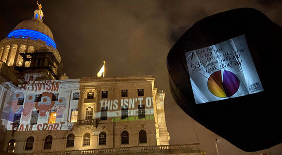 An image capturing the projections on the State House and on a black hot air balloon at the May 3 rally organized by The Womxn Project.