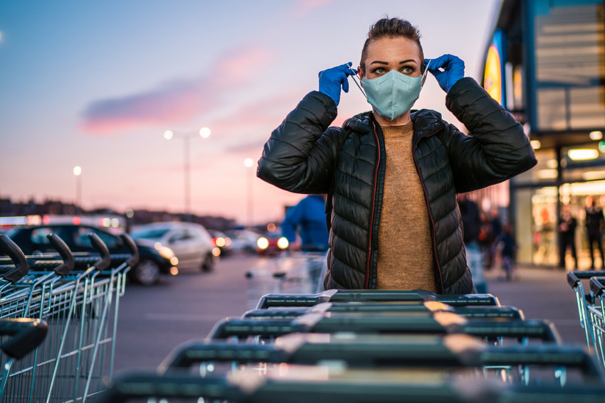 Woman with protective gloves puts a medical mask on her face as a virus protection in a supermarket parking lot.