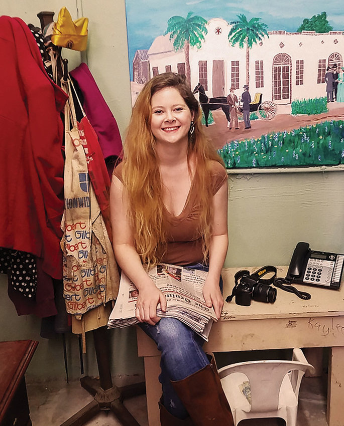 Kayleen Holder with her old writing desk built by her grandfather Pat DuBose. In the background is a painting depicting the family tale of her Great-Great Grandfather W.L. DuBose, who traded a brand-new horse and buggy for the newspaper business in 1897. 