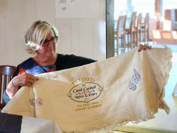 Daily News director of advertising Carol Cutshall displayed a blanket given to her as a retirement gift. After 42 and one-half years, Cutshall retired from her position April 28. (Becky Weikert/The Daily News)