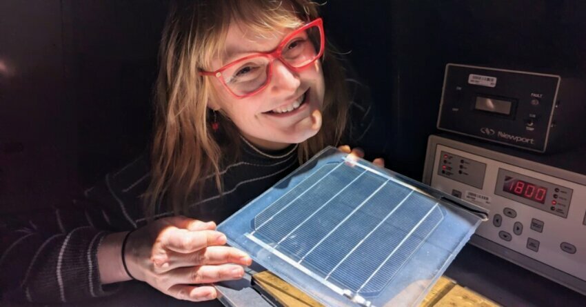 Girl with orange glasses at SUNLAB smiling holding a square solar test. 