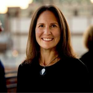 Emily Pierce Persefoni Woman smiling with brown hair and a black shirt on