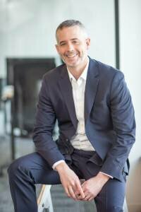 Mark Danzenbaker Sitting on a stool. Man wearing a grey suit