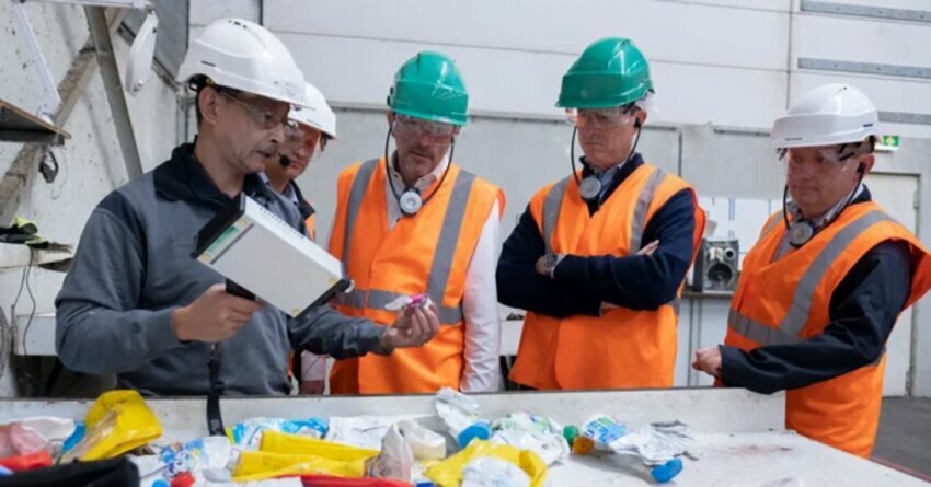 Men in hard hats and orange protective wear at a plastic recycling plant