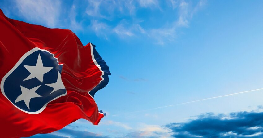 A red Tennessee state flag is pictured against a blue sky with some white clouds.