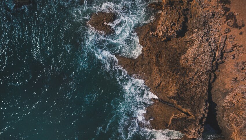 An overhead shot of ocean meeting rocky shore