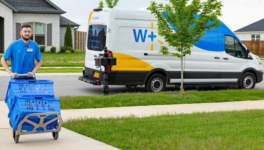 A white Walmart delivery man wearing a blue shirt pushes a blue cart up a driveway.