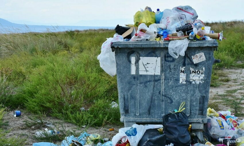 Plastic waste in a collection bin with more waste scattered on the ground.