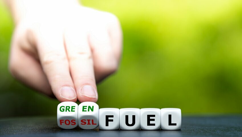 Two white fingers prop up dice that spell out "green." Four dice adjacent spell out "fuel."