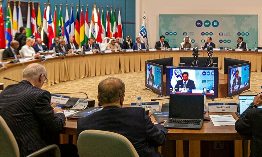 Multiple world leaders sitting around a table discussion, country's flags in the background