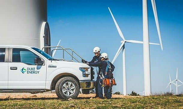 two men in hard hats work near a truck at a wind turbine facility