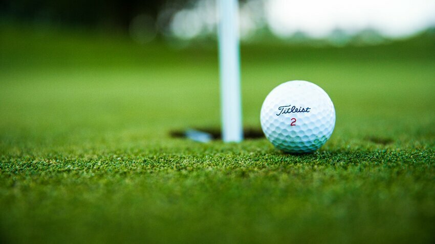 white golf ball is poised to roll into the cup