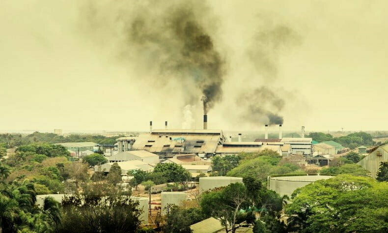 A smoke stack in the distance polluting in a town