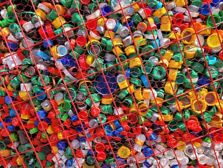 colored plastic bottle tops load down a metal mesh container.