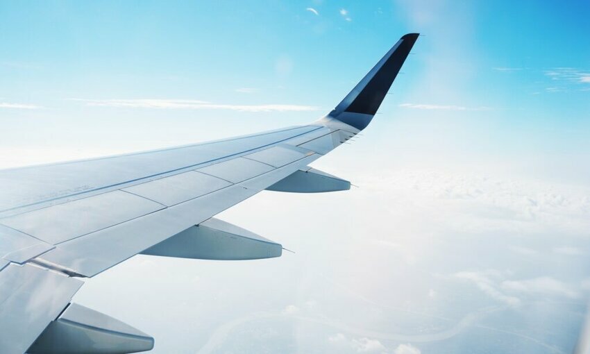 Wing of a plane flying in the sky with clouds below