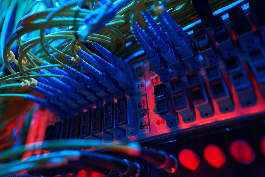 blue fiber optic cables inserted into ports of switch panel inside server rack