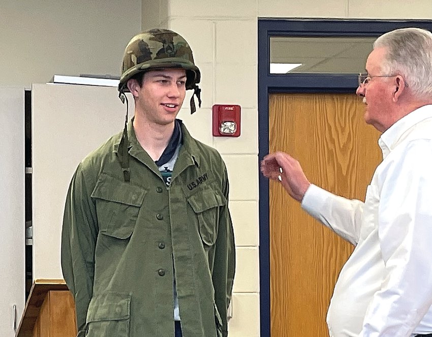 River Ridge senior Caden Albrecht dons a military uniform as Vietnam War veteran Steve Townsend explains the equipment. Members of Vietnam Veterans of America visited Mike Dittmar&rsquo;s history classroom at River Ridge High School on April 11 to answer questions the Vietnam War and what students should learn from their study of the war.