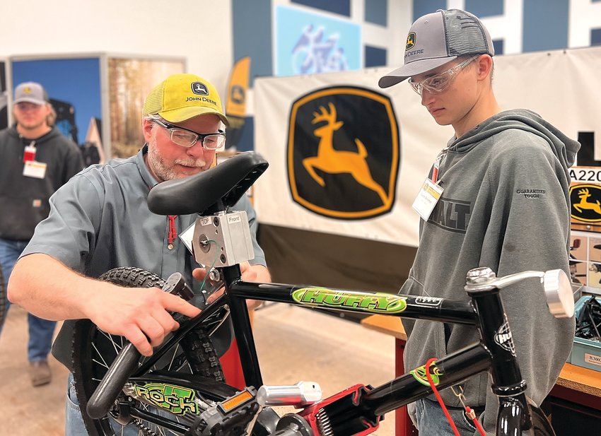 Pete Vincent, of John Deere Dubuque Works, works with East Dubuque senior Dustin Shireman during the school&rsquo;s participation in the John Deere bike build earlier this month.