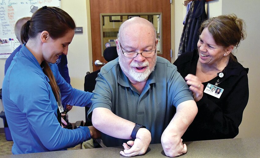 Midwest Medical Center physical therapists Sara Doerr, left, and Julie Soat, right, are obviously thrilled after Steve Holmes walks five-and-a-half feet from wheelchair to the counter. After putting in so much effort, Holmes had to catch his breath.