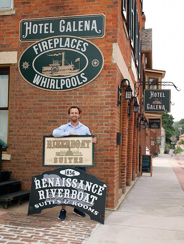 Nate Gawlik poses with the new and old signage for the Riverboat Suites/Hotel Galena.