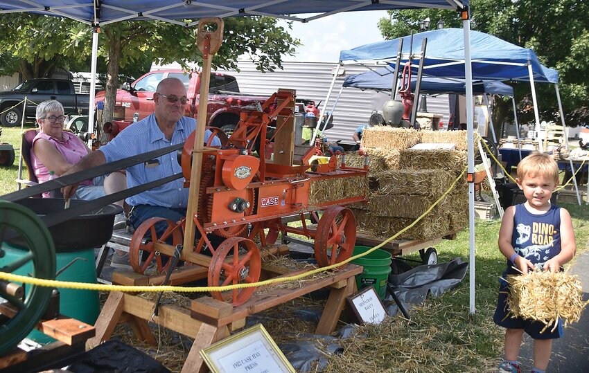 The oldest community fair in Illinois held its 102nd annual event with three days of festivities from Friday, July 21 through Sunday, July 23. Here, Ivan Offenheiser, 3, Elizabeth, holds a freshly-made bale of straw from the 1/3 scale model 1922 Case hay press. Bill Hayes, middle, operates the Woodbine Service Garage in Woodbine and built the model over the past winter. Bill&rsquo;s wife, Jocelyn, is in the back.