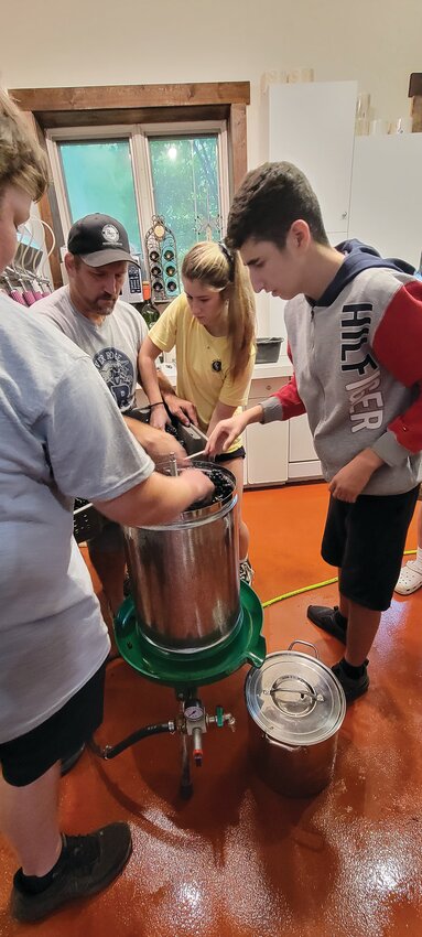 Sawyer Fry, vineyard owner Kyle Soahn, Leah Spahn and Loran Ahmedi work together to pour the grapes into the juicer.