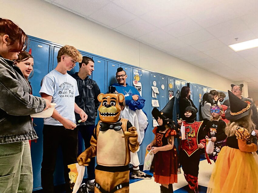 Left: River Ridge High School teacher Dennis Downs high fives Jayyda Stevenson, third grader, who was one of the students parading through the building in full Halloween gear last week. Right: River Ridge High School students Natalie Keleher, Faith Morhardt, Hamish Boden, Damon Dittmar and Matthew Ransom hand out candy to the elementary school students who dressed for Halloween.