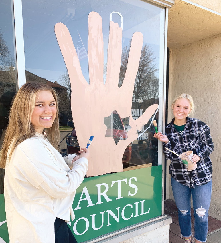 EAST students Jaycee Paxton (left) and Chloe Hooten from Harrison High School paint windows Thursday in front of businesses in downtown Harrison to help bring awareness for Child Abuse Awareness Month for April. Other EAST students involved were Gavin Coker, Lea Grantz, Liam Bright, Lucas Paul and Destinee Olson.
