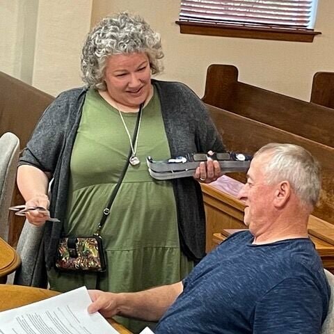 Newton County Library Director Kenya Windel offers a pair of solar eclipse glasses to Newton County Justice of the Peace Richard Campbell prior to the start of Monday night's quorum court meeting. Many local libraries are offering free glasses to be used for viewing the eclipse safely. JEFF DEZORT / STAFF