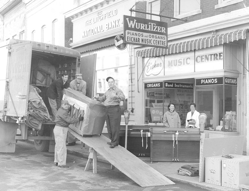 Gene and Charlotte Eichar, professional musicians and music educators, opened Eichar Music Centre at 108 West Ryder Street in 1958. In this photo from the 1960s, Mrs. Charlotte Eichar stands in front of Eichar Music Centre (at left) overseeing an inventory of Wurlitzer pianos as it is being unloaded.