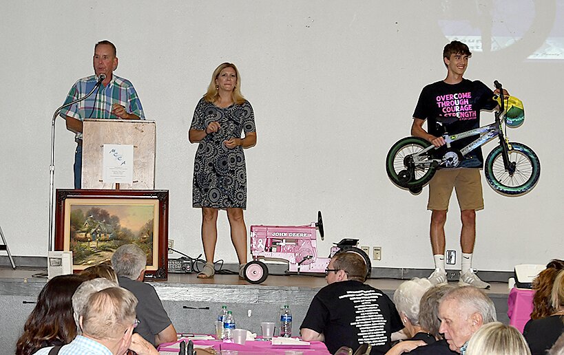 As Hal Langheim of Langheim Auctioneers watches for bidders, grant recipient Reece Lohman holds up a bike for the auction. Also pictured is emcee Nikki Bishop, center.
