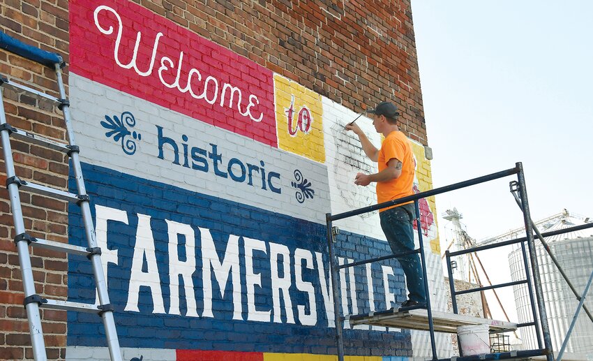 Dan Ricketts of St. Louis Sign and Mural Company works on a postcard mural on The Opera House building in downtown Farmersville on Thursday, Oct. 12. The new addition is part of the Route 66 Postcard Mural Trail. Also helping to paint the mural was Mike Meyer.