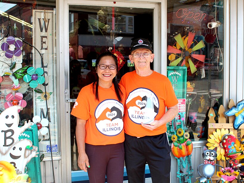 Ross and Marie Owens, owners of The Holiday Shop, proudly stand in front of their building while Ross holds his 2024 Transplant Olympics Athlete award.