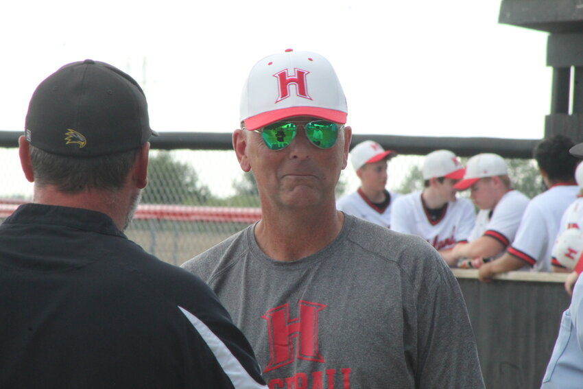 The pregame meeting between coaches and umpires is caught in the reflection of the shades worn by Highland Head Baseball Coach, and former University of Iowa pitching star, Allen Rath.