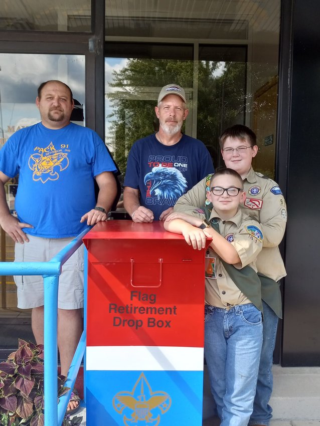 Scout Master for Troop 91B Richard Bell (left) stands with James Gagne (right) and his two scouts, Vaughn and Scot Gagne, with one of the two new retired flag drop boxes. Bell shares how the idea came to him, &ldquo;I had seen that many different Scout Troops across the country have set up drop boxes for retired flags&hellip;So I thought this would be simpler for everybody involved.&rdquo;