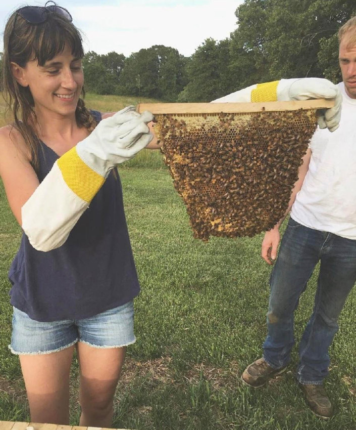Whitney Stevens, a local beekeeper checks her hives while her husband stands by. Stevens, who keeps Top Bar and Langstroth hives, started beekeeping in 2018 with her Dad.