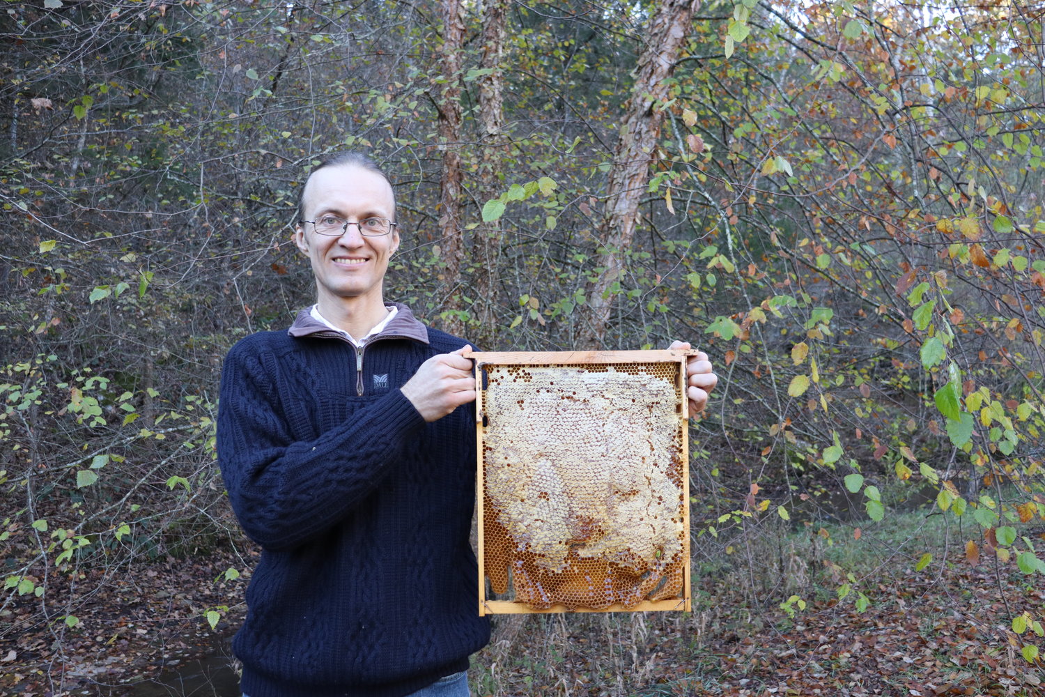 Dr. Leo Sharashkin is seen here with one of his hives from a horizontal hive box. He mentions that because this method does not aggravate the bees, “There is little defensive response from the bees that I can open my hives without any protection. My children help me without any protective jackets. It is not because I’m a special person or a bee whisperer. No, if you do not disturb the bees, they have no reason to strike back”.