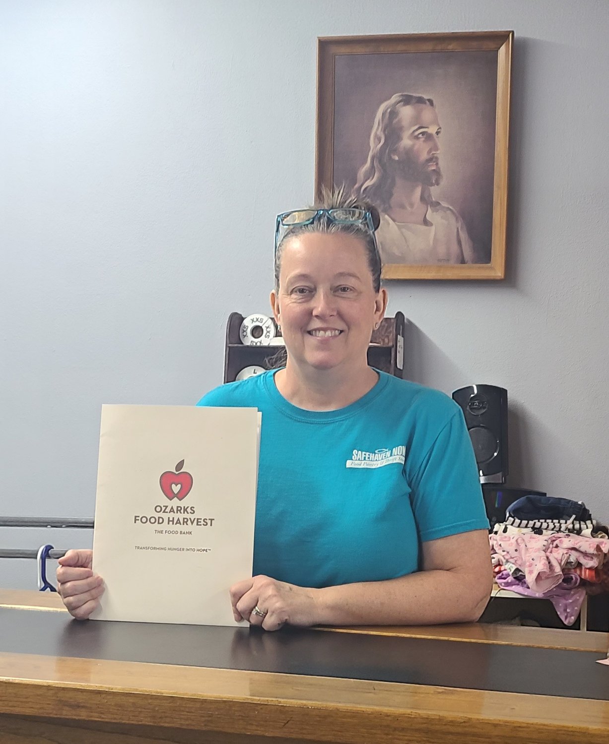 Tina Viebrock becomes Safe Haven Now of Fordland’s newest store manager. Viebrock presents a folder containing the organization’s acceptance letter from Ozark’s Food Harvest, an important moment in Safe Haven’s history.