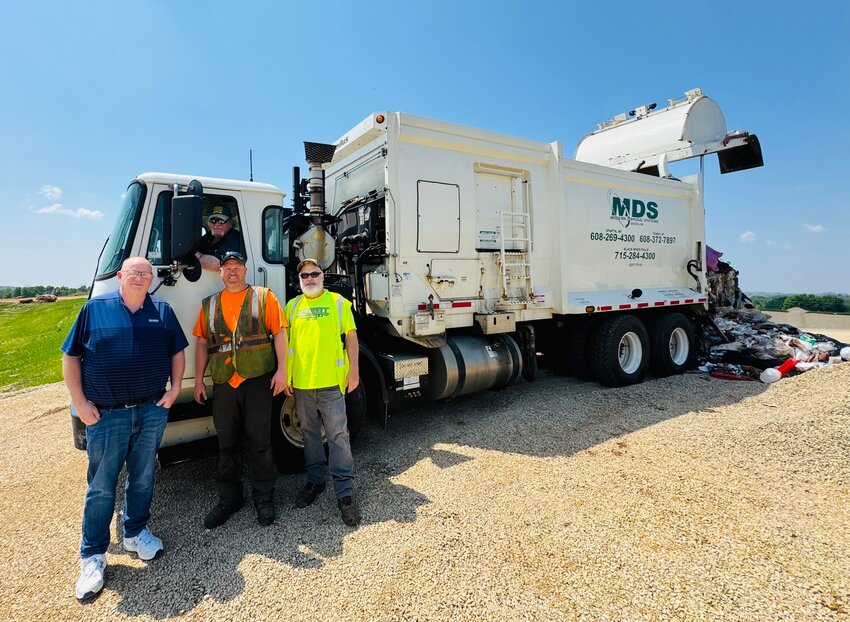 Modern Disposal Owner Jerry Martell, sitting in the garbage truck, dumped the first load of garbage into Monroe County’s new landfill cell June 4. From front left: Monroe County Chairperson Cedric Schnitzler, Modern Disposal Employee and Jerry’s son, Michael Martell, and Riverview Construction Landfill Operator Terry Taylor stand next to the Modern Disposal Systems truck as it empties the first load into the new landfill expansion cell.