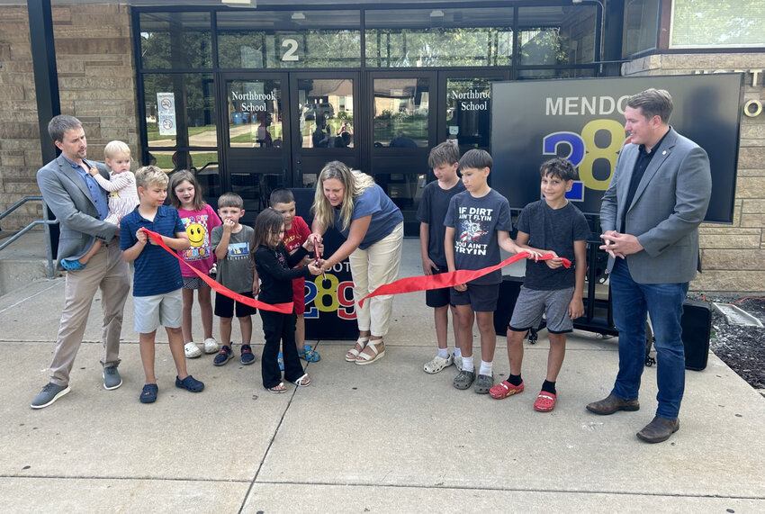 Mendota Elementary School District 289 Board president Theresa Komitas helps young school children cut the ribbon during a ceremony for the completion of the district’s solar project in which panels were installed on the roof of all three schools. Looking on are eighth grade science teacher Jordan Zoelzer, left, and Rep. Brad Fritts, right. (Reporter photo)