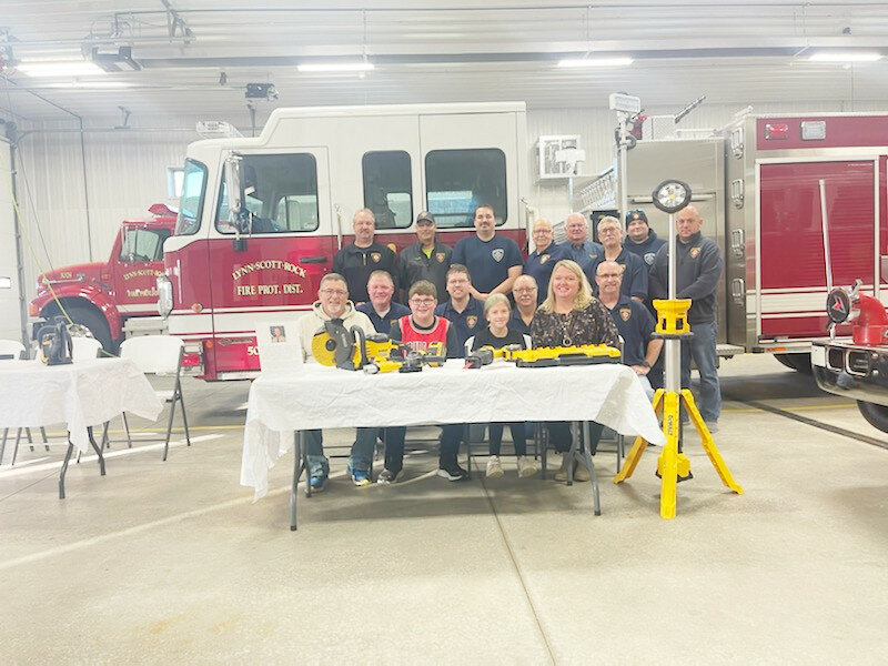 Seated at the table from left to right are Mike Bowers (Scott’s dad), Brayden Bowers (Scott’s son), Brooklyn Bowers (Scott’s daughter) and Melissa Bowers (Scott’s wife). Members of the Lynn-Scott-Rock Fire Protection District are standing and kneeling.
