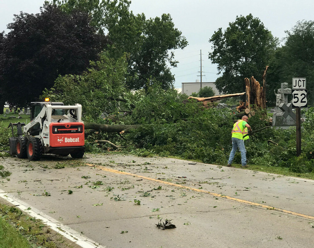 Workers clean up debris from a fallen tree that blocked Illinois Route 251 at the Holy Cross Cemetery. (Reporter photo)