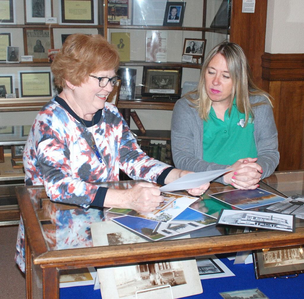 Chris Stamberger, left, of the Mendota Museum & Historical Society, and Shelby Weide of the Mendota Area Chamber of Commerce look over some photos from the collection at Hume Carnegie Museum. MMHS and the Chamber are sponsoring a photography contest, “Capture Our Town.” (Reporter photo)